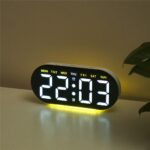 Réveil numérique LED grand affichage 18 cm noir avec éclairage ambiant jaune, posé sur une table dans une pièce.